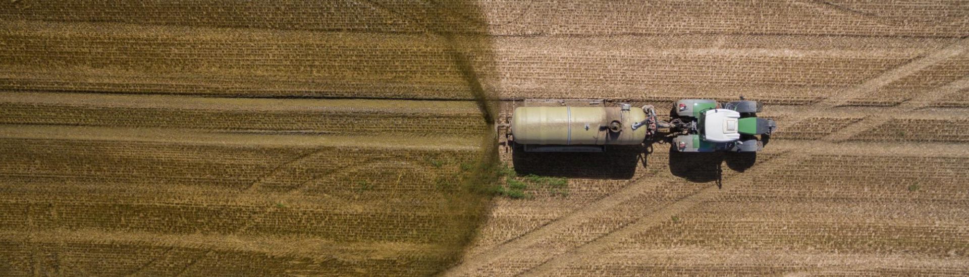 aerial view of a tractor with a trailer fertilizes a freshly plowed agriculural field with manure in germany