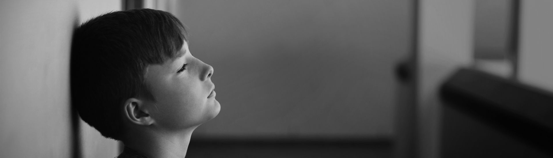 Sad schoolboy leaning head against wall in corridor