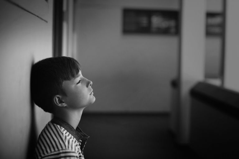 Sad schoolboy leaning head against wall in corridor