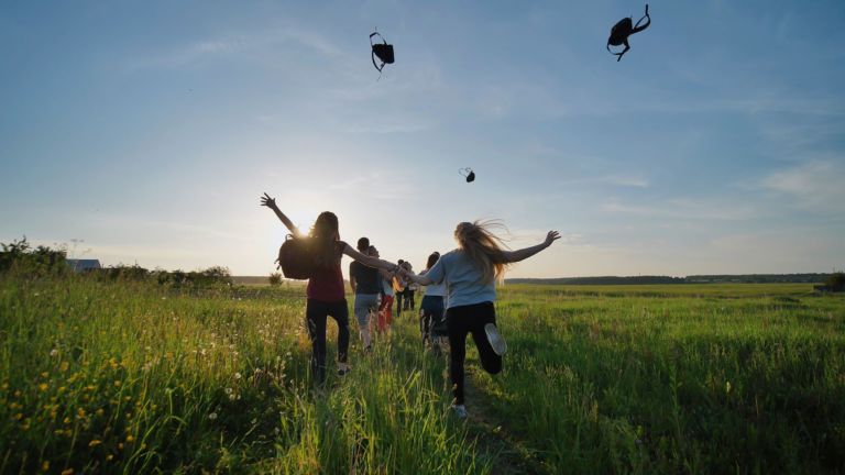 Happy senior pupils flee and toss their portfolios against the sunset. Happy ending school days. Slow motion.