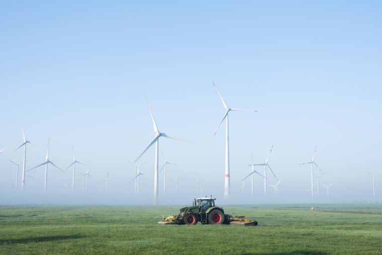 farmer mows grass near wind turbine farm in oastfriesland on misty summer morning