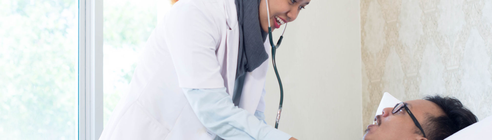Muslim Female doctor and her male patient inside hospital clinic room doing examination with stethoscope