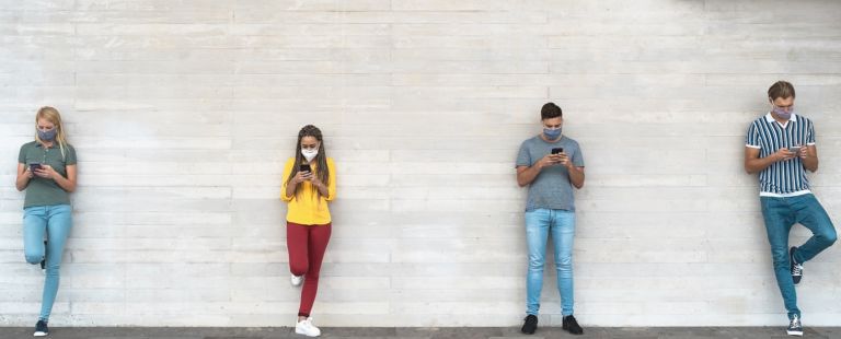 Young people wearing surgical mask using mobile phone keeping social distance – Millennial friends watching media trends on smartphones during corona virus outbreak – Youth and technology concept