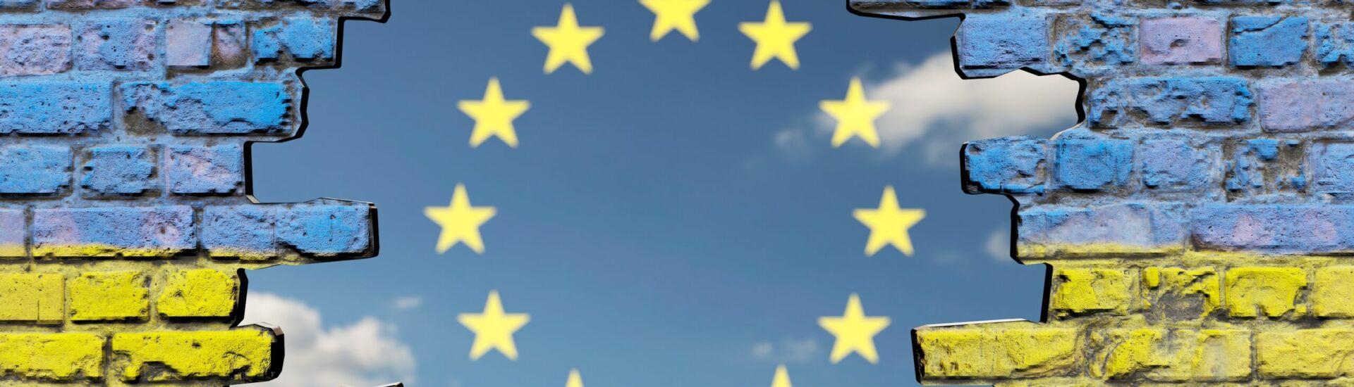 Loch in Mauer mit Ukraine-Fahne vor Himmel mit EU Sternen