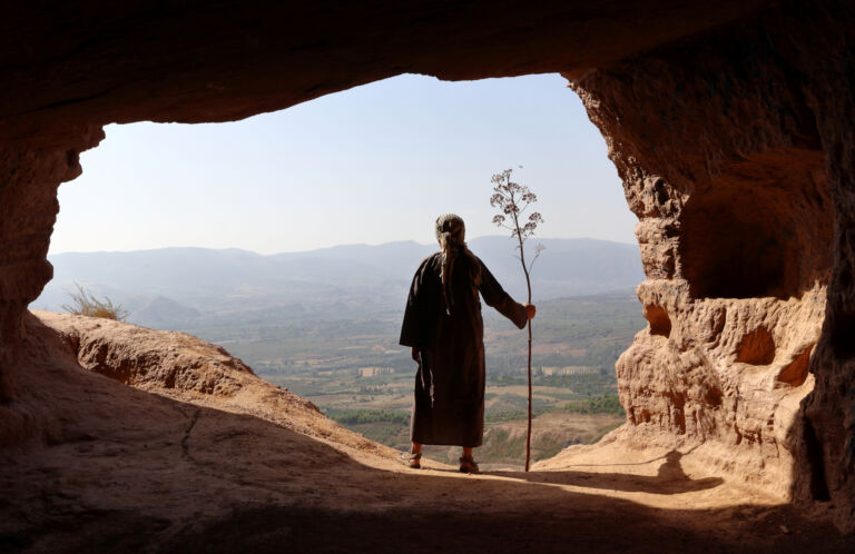 HERMIT  MAN LOOKING TO THE VALLEY FROM A HIGH CAVE WITH A BRANCH