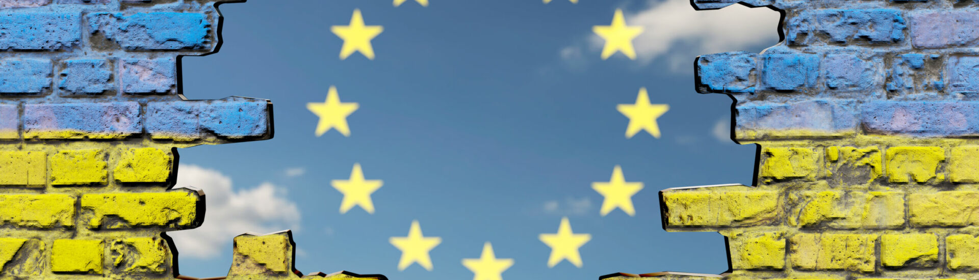 Loch in Mauer mit Ukraine-Fahne vor Himmel mit EU Sternen
