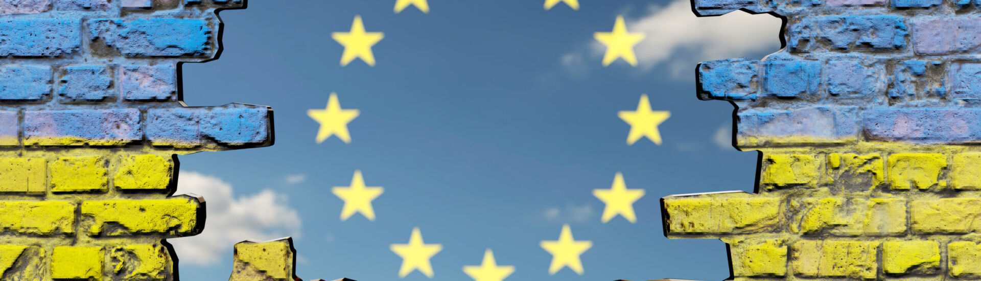Loch in Mauer mit Ukraine-Fahne vor Himmel mit EU Sternen