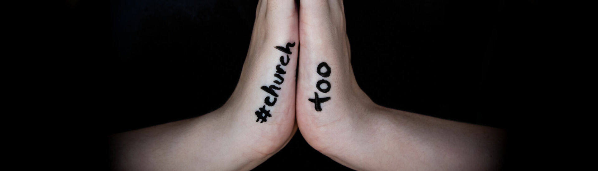 Woman holding hands in prayer with hashtag #churchtoo written on hands to protest the cover up of sexual assault in churches