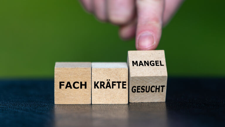 Hand dreht Würfel und ändert den Ausdruck ‚Fachkräfte gesucht‘ in ‚Fachkräftemangel‘.