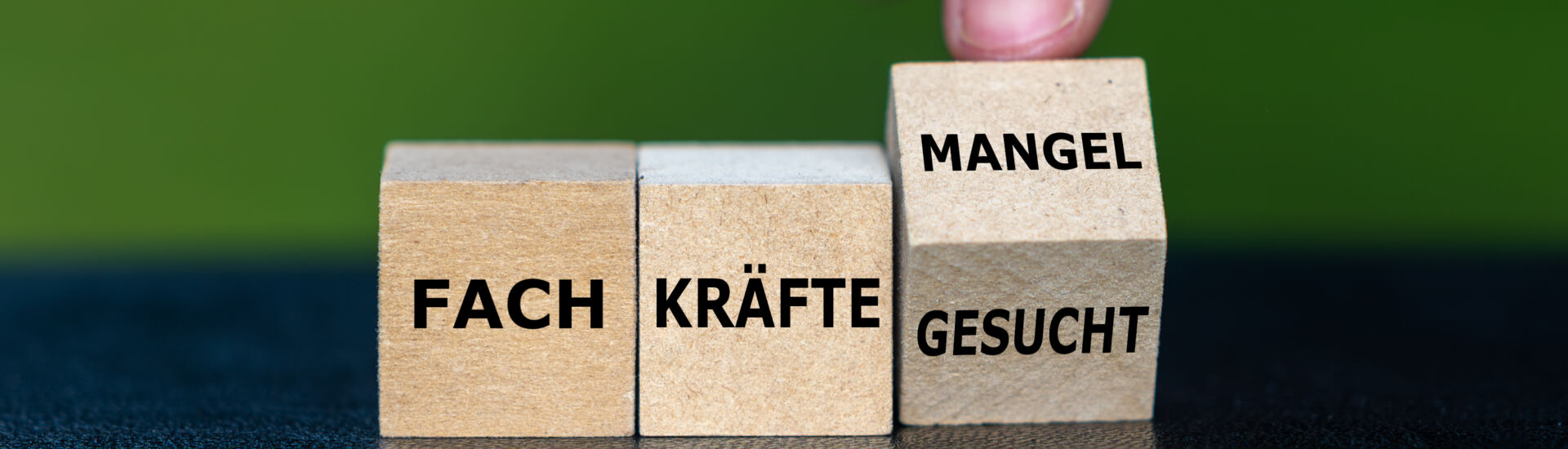 Hand dreht Würfel und ändert den Ausdruck ‚Fachkräfte gesucht‘ in ‚Fachkräftemangel‘.