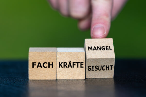Hand dreht Würfel und ändert den Ausdruck ‚Fachkräfte gesucht‘ in ‚Fachkräftemangel‘.