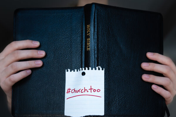 Woman holding Holy Bible with #churchtoo hashtag written on cover