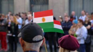 Two flags of Kurds hold by adult woman and men, standing on their back, during street protest against Turkish invasion in Syria, in background other protesters in soft focus