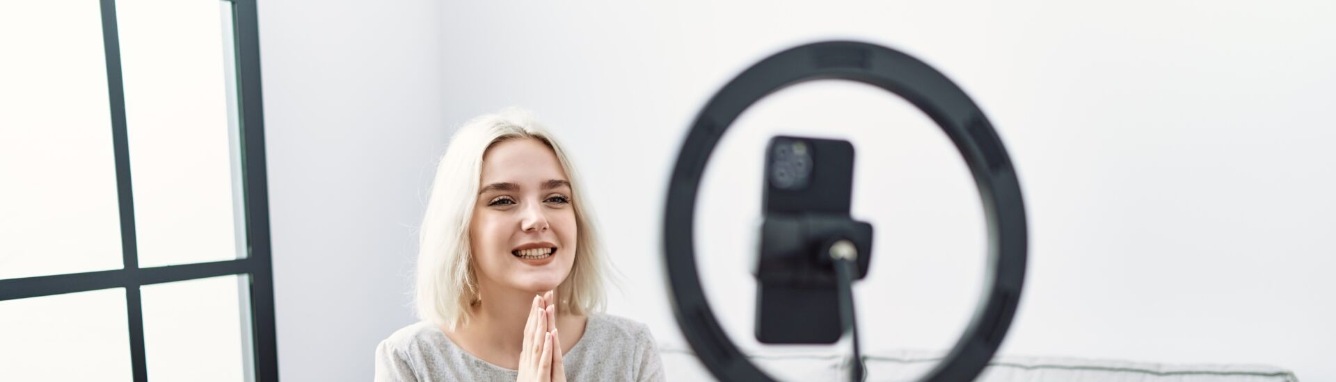 Young caucasian woman recording vlog tutorial with smartphone at home praying with hands together asking for forgiveness smiling confident.